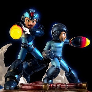 May include: A dynamic figurine featuring two characters in blue and black armor, poised in action poses. One figure holds a glowing yellow energy ball, while the other has a red and yellow energy cannon. The figures stand on a detailed base with a black background.