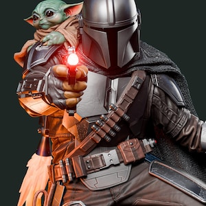 May include: A detailed figurine of The Mandalorian holding a blaster with a red light, with Grogu, also known as Baby Yoda, in his arms. The Mandalorian wears a silver helmet and armor, with a brown belt and pants. Grogu is wrapped in a brown cloth.