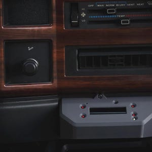 Peut inclure: Une console centrale de tableau de bord de véhicule avec une finition en grain de bois, des curseurs de climatisation noirs marqués OFF, MAX, NORM, BI-LEV, VENT, HEAT, et un allume-cigare. Un module électronique gris avec quatre voyants rouges est fixé en dessous.