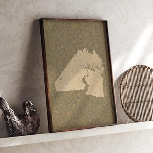 Può includere: Una stampa rettangolare incorniciata che presenta una sagoma di mappa beige di una massa terrestre con dettagli intricati di fiumi o coste, su uno sfondo verde oliva scuro coperto da un motivo denso e ripetitivo di piccoli motivi floreali giallo oro.