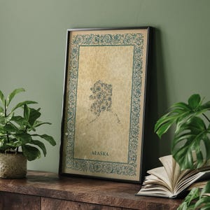 Puede incluir: Una impresión rectangular enmarcada con un fondo beige texturizado y un borde floral de color verde azulado oscuro. En el centro, el contorno del estado de Alaska en verde azulado está lleno de patrones florales, con la palabra ALASKA debajo.