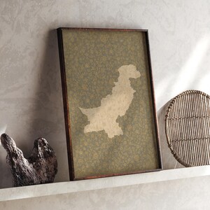 May include: A rectangular framed wall art piece featuring a beige silhouette map of Pakistan centered on a dark olive green background with a dense, repeating pattern of small, intricate golden floral motifs throughout the entire print.