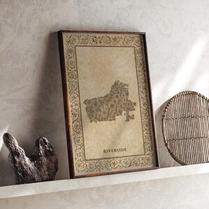 May include: A rectangular framed print featuring a map of Riverside with a floral pattern overlay on a beige background. The frame is dark brown wood, and the border of the print is decorated with an intricate, repeating vine and leaf design.