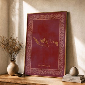 Op de afbeelding: Een rechthoekige ingelijste kunstdruk met een dieprode achtergrond en een gouden kaart van Indonesië in het midden. De print bevat een decoratieve gouden bloemenrand en het woord INDONESIA in gouden letters aan de onderkant.