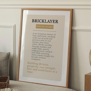 Könnte beinhalten: Ein gerahmter Druck mit dem Wort "BRICKLAYER" in fetten schwarzen Buchstaben oben. Der Druck hat einen beigefarbenen Hintergrund mit Text, der den Beruf beschreibt. Der Rahmen ist aus Holz.