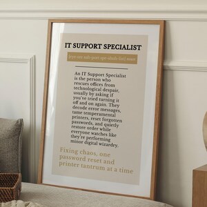 May include: A framed print with the text "IT SUPPORT SPECIALIST" in a bold font. The print has a beige background with black text describing the role of an IT Support Specialist. The frame is a light brown color.
