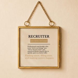 May include: A square wall hanging in a gold metal frame with a chain, featuring the definition of the noun RECRUITER. The text reads: Professional matchmaker who turns we're not hiring into when can you start and finding talent, filling seats.