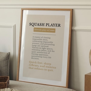 May include: A framed wall art print featuring a dictionary-style definition of a squash player. The text is printed in black and gold on a beige background, detailing the characteristics of a squash player with a light wood frame border.