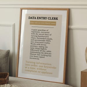 May include: A framed print with the words "DATA ENTRY CLERK" in bold letters. The print has a beige background with text describing the role of a data entry clerk. The frame is made of wood.
