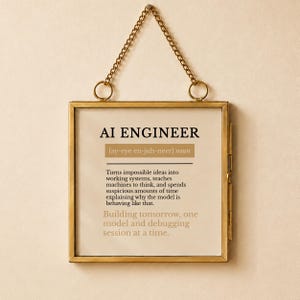 May include: A square wall hanging in a gold metal frame with a chain, featuring a printed definition of AI ENGINEER. The text reads: AI ENGINEER [ay-eye en-juh-neer] noun. Turns impossible ideas into working systems, teaches machines to think, and spends suspicious amounts of time explaining why the model is behaving like that. Building tomorrow, one model and debugging session at a time.