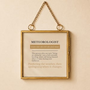 Könnte beinhalten: Ein quadratischer Wandbehang mit einem dünnen Messingrahmen und einer goldenen Kette. Der Druck zeigt das Wort METEOROLOGIST, seine phonetische Aussprache und eine humorvolle Definition über das Vorhersagen von Wetter und Entschuldigungen.