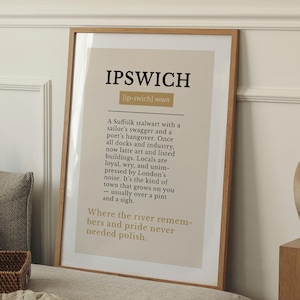 May include: A framed print with the word "IPSWICH" in bold black letters at the top. Below, a definition of Ipswich is written in black text on a beige background. The frame is made of light brown wood.