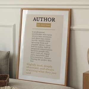 May include: A framed print featuring the definition of "AUTHOR" in black text on a beige background. The wooden frame surrounds the text, which describes the characteristics of an author.