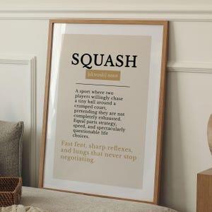 May include: A framed wall art print featuring a dictionary-style definition of the word SQUASH. The text is printed in black and gold on a beige background, describing the sport with humour, including the phrase Fast feet, sharp reflexes.