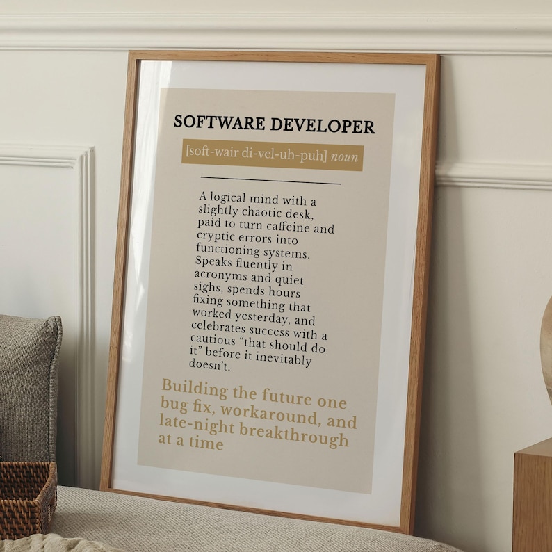 May include: A framed print with the text "SOFTWARE DEVELOPER" and a definition. The definition describes a software developer's work habits and mindset. The frame is a light brown colour.