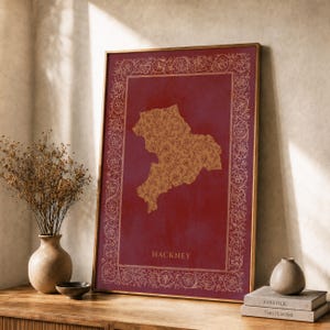 Könnte beinhalten: Ein gerahmter vertikaler Wandkunstdruck mit einem tiefroten Hintergrund und einer zentralen Landkartenform von Hackney, die mit einem goldenen Blumenmuster gefüllt ist. Der Druck ist von einer goldenen floralen Bordüre umgeben und enthält den Text HACKNEY.