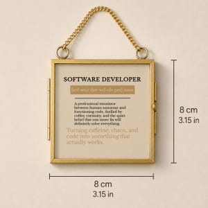K&ouml;nnte beinhalten: Ein quadratischer goldfarbener Metallrahmen mit einer Aufh&auml;ngungskette, der 8 cm mal 8 cm misst. Der Druck zeigt die Definition eines Softwareentwicklers, der als professioneller &Uuml;bersetzer zwischen menschlichem Unsinn und Code fungiert.