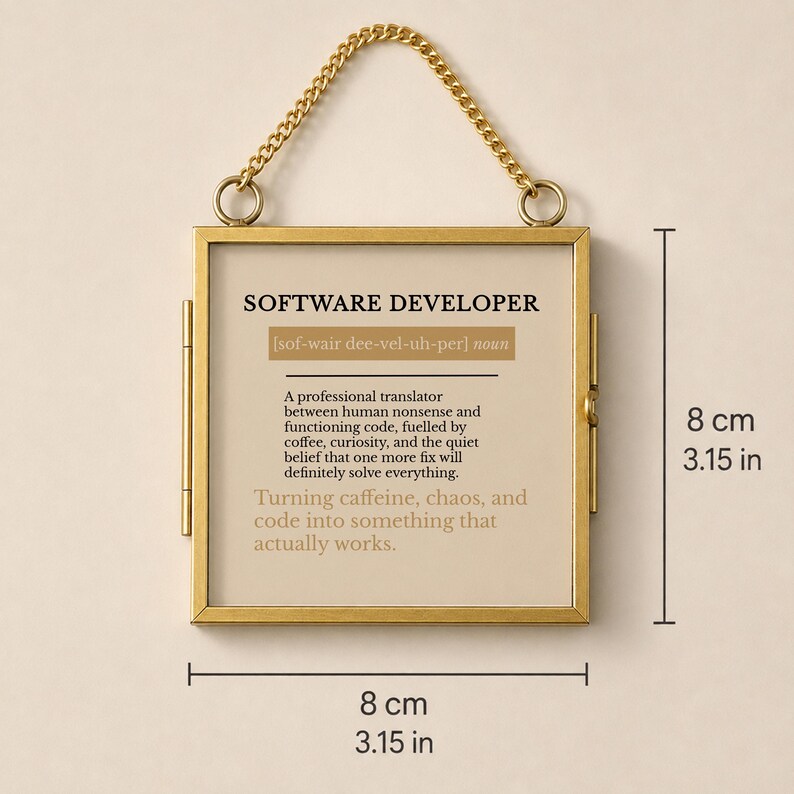 K&ouml;nnte beinhalten: Ein quadratischer goldfarbener Metallrahmen mit einer Aufh&auml;ngungskette, der 8 cm mal 8 cm misst. Der Druck zeigt die Definition eines Softwareentwicklers, der als professioneller &Uuml;bersetzer zwischen menschlichem Unsinn und Code fungiert.