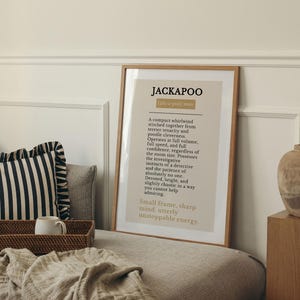 Pu&ograve; includere: Una stampa artistica da parete incorniciata con la parola JACKAPOO in grassetto nero, seguita da un paragrafo descrittivo sulla razza canina, stampata su sfondo beige chiaro con una sottile cornice in legno in un ambiente neutro.