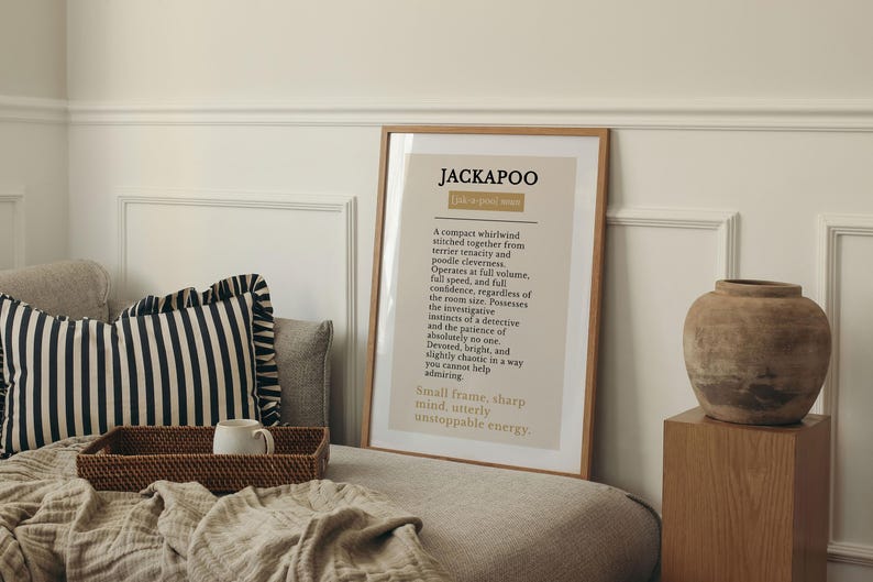 Pu&ograve; includere: Una stampa artistica da parete incorniciata con la parola JACKAPOO in grassetto nero, seguita da un paragrafo descrittivo sulla razza canina, stampata su sfondo beige chiaro con una sottile cornice in legno in un ambiente neutro.