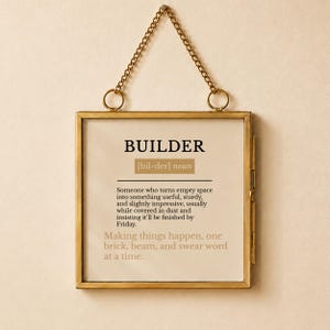 Könnte beinhalten: Ein quadratischer, messingfarbener Metallrahmen, der an einer passenden Kette hängt. Der Rahmen enthält einen Druck mit dem Wort BUILDER, seiner phonetischen Aussprache und einer Definition, die jemanden beschreibt, der leeren Raum nützlich macht.