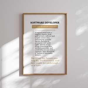 May include: A framed print with the text "SOFTWARE DEVELOPER" in black, with a definition below. The definition describes a software developer's work habits and mindset. The frame is a light brown colour.