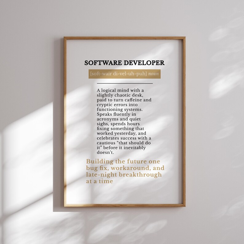 May include: A framed print with the text "SOFTWARE DEVELOPER" in black, with a definition below. The definition describes a software developer's work habits and mindset. The frame is a light brown colour.