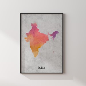 May include: A framed wall art print featuring a watercolour map of India in shades of pink, orange, and purple against a textured grey background. The word India is printed in a black script font at the bottom centre of the rectangular artwork.