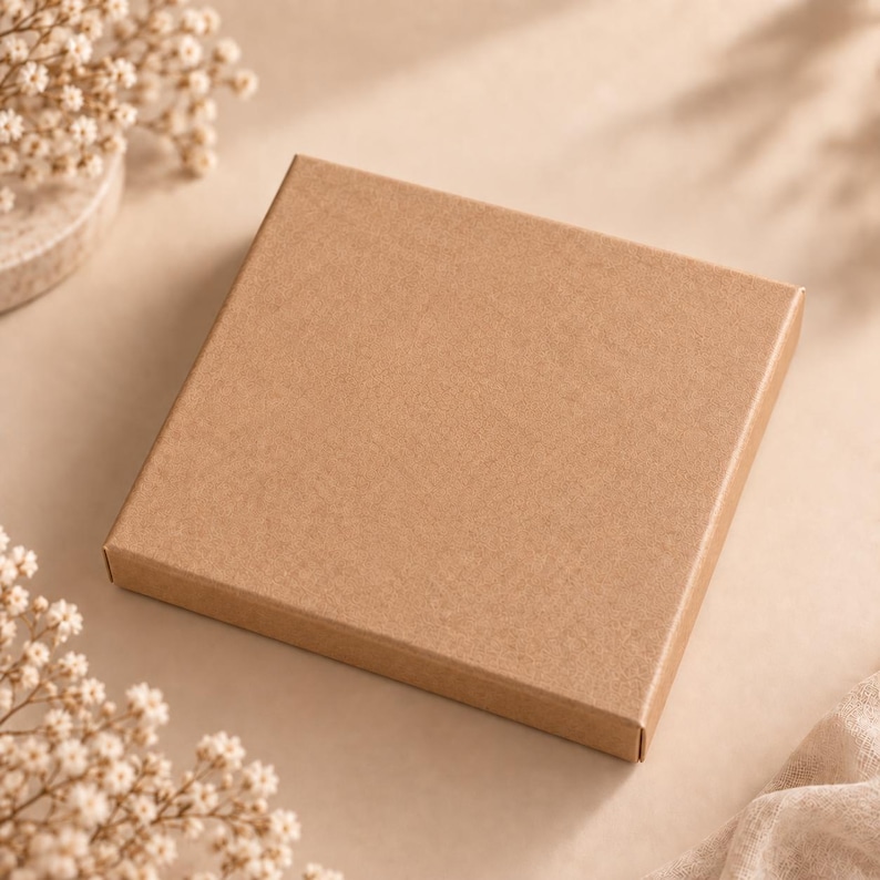 May include: A square, flat, light brown cardboard gift box with a smooth, matte finish. The box is closed and features a simple, clean design with sharp, straight edges, presenting a neutral appearance suitable for various small items.