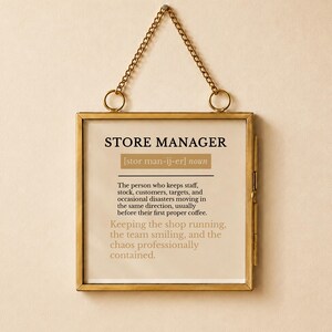 May include: A square wall hanging sign in a gold metal frame with a chain, featuring the definition of a store manager. The text reads: STORE MANAGER [stor man-ij-er] noun. The person who keeps staff, stock, customers, targets, and disasters moving.