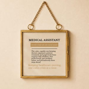 Op de afbeelding: Een vierkante, messingkleurige metalen lijst met een ophangketting met een gedrukte definitie van een medisch assistent. De tekst luidt: MEDICAL ASSISTANT [med-i-kal uh-sis-tant] noun. The calm, capable one keeping doctors organised.