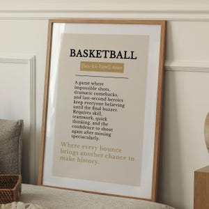 May include: A framed wall art print featuring a dictionary-style definition of the word BASKETBALL in black text on a beige background. The text includes the phonetic spelling, noun classification, and a descriptive paragraph about the sport.