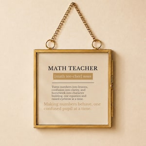 May include: A square brass-toned metal frame with a hanging chain containing a printed definition of a math teacher. The text reads: MATH TEACHER [math tee-cher] noun. Turns numbers into lessons, confusion into clarity, and homework into character building, one equation and raised eyebrow at a time. Making numbers behave, one confused pupil at a time.