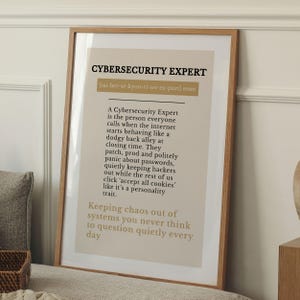 May include: A framed print with the text "CYBERSECURITY EXPERT" in black, with a definition below. The print has a light beige background and a wooden frame. The text describes the role of a cybersecurity expert.