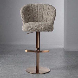 May include: A modern bar stool with a textured, light gray seat and backrest. The seat is supported by a bronze-colored metal stem and base. The stool has a footrest and an adjustable height mechanism.