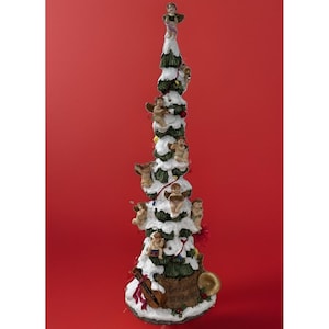 Pode incluir: Uma estatueta de árvore de Natal alta e cónica com ramos verdes cobertos de neve branca. A árvore está decorada com várias figuras pequenas de querubins, um violino e uma trompa dourada. A base é castanha com um padrão de notas musicais.