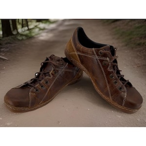 May include: A pair of brown leather shoes with white stitching and laces. The shoes have a worn, textured appearance, suggesting durability and a vintage aesthetic. The shoes are designed for comfort and casual wear.