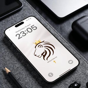 May include: A smartphone displays a lion illustration with a crown and the text "Revelation 5:5" on the screen. The time is 23:05 on Wednesday, April 15. Other items include a laptop, pencil, and wireless earbuds.