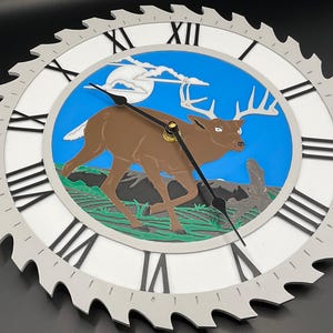 May include: A round wall clock with a saw blade-style outer edge. The clock face features a brown deer in a blue and green landscape. Black Roman numerals mark the hours. The clock hands are black.
