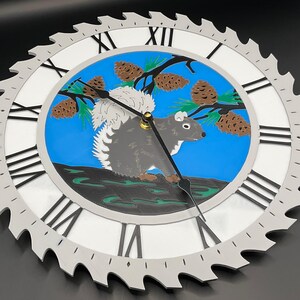 May include: A unique wall clock with a circular design. The clock face features a gray squirrel, pine cones, and a blue background. The clock's outer edge is shaped like a saw blade, with Roman numerals marking the hours.