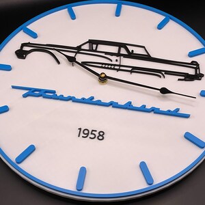 May include: White wall clock with a blue border and blue hour markers. The clock features a black car silhouette, the word "Thunderbird" in blue, and the year "1958". The clock hands are black and gold.