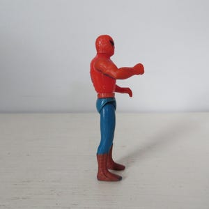 May include: A red and blue plastic action figure of Spider-Man. The figure is posed with its right arm raised and its left hand on its hip.