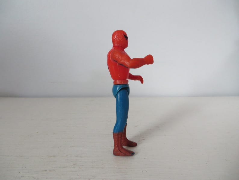 May include: A red and blue plastic action figure of Spider-Man. The figure is posed with its right arm raised and its left hand on its hip.
