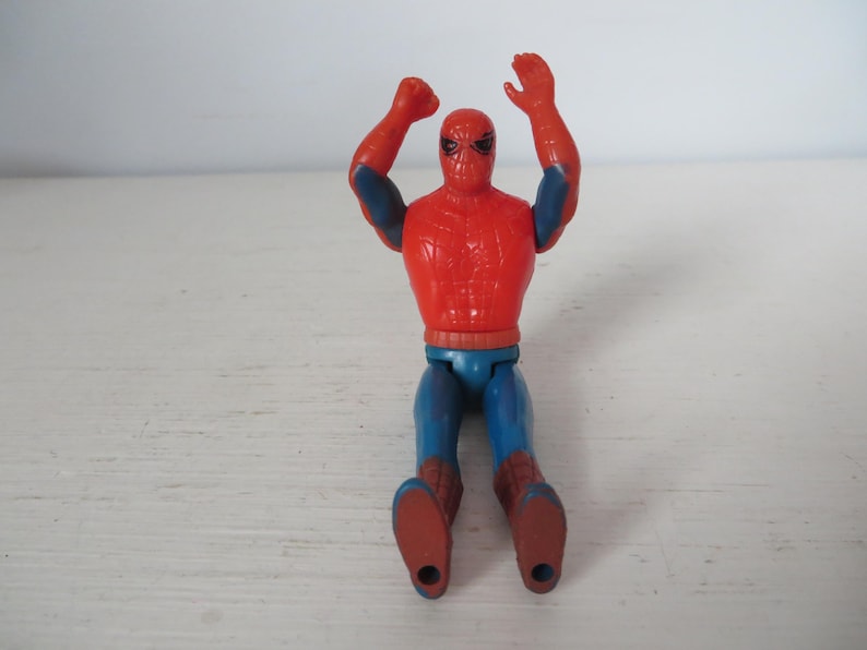May include: A red and blue plastic action figure of Spider-Man with his arms raised in the air. The figure has a red and blue suit with a spider logo on the chest.