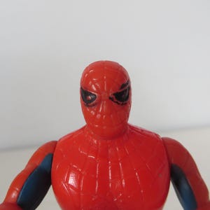 May include: A red and blue plastic action figure of Spider-Man. The figure has a detailed face with black eyes and a red and blue suit with a spider web design.