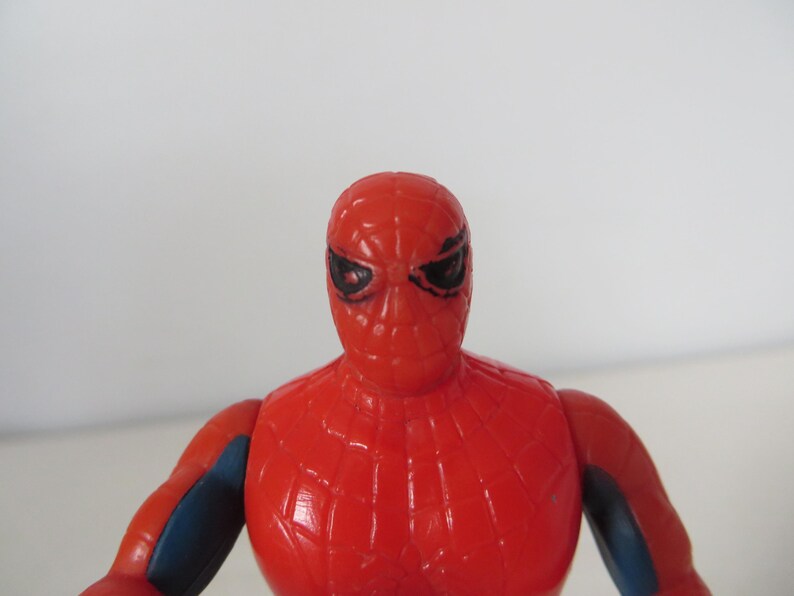 May include: A red and blue plastic action figure of Spider-Man. The figure has a detailed face with black eyes and a red and blue suit with a spider web design.