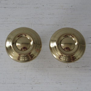 May include: Two gold-toned round cabinet knobs with a raised, concentric circle design.