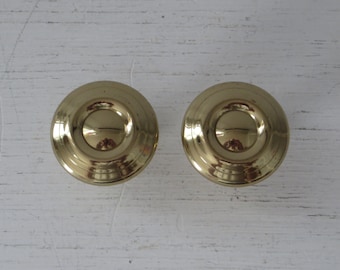 May include: Two gold-toned round cabinet knobs with a raised, concentric circle design.