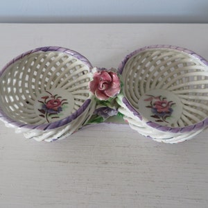 May include: A white ceramic double basket with a woven design and floral accents. The baskets are connected by a floral design with a pink rose in the center.
