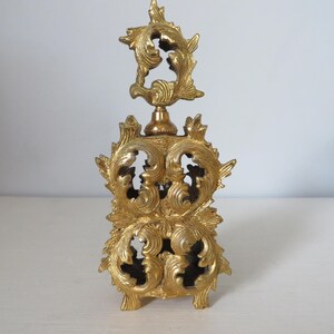 May include: Ornate gold-colored perfume bottle with intricate, swirling leaf and floral designs. The bottle has a decorative top and a rectangular base. The overall design is vintage and elegant, suitable for display or use.